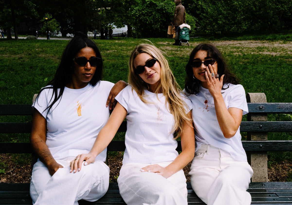 Three women in white outfits sitting on a bench in a park.
